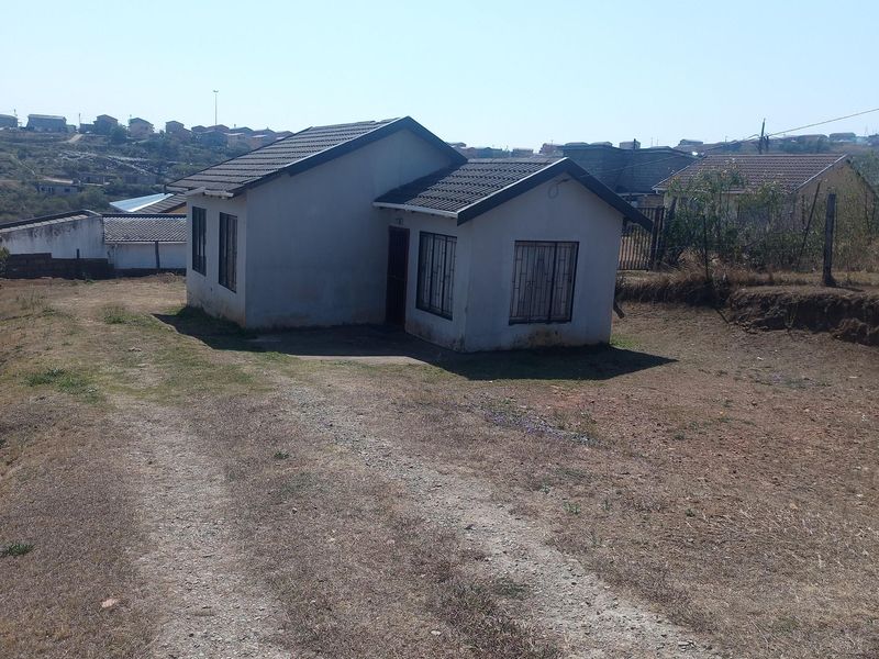 A detached single-story house featuring a tiled roof and security bars on windows, situated on a large, unlandscaped plot with a gravel driveway.