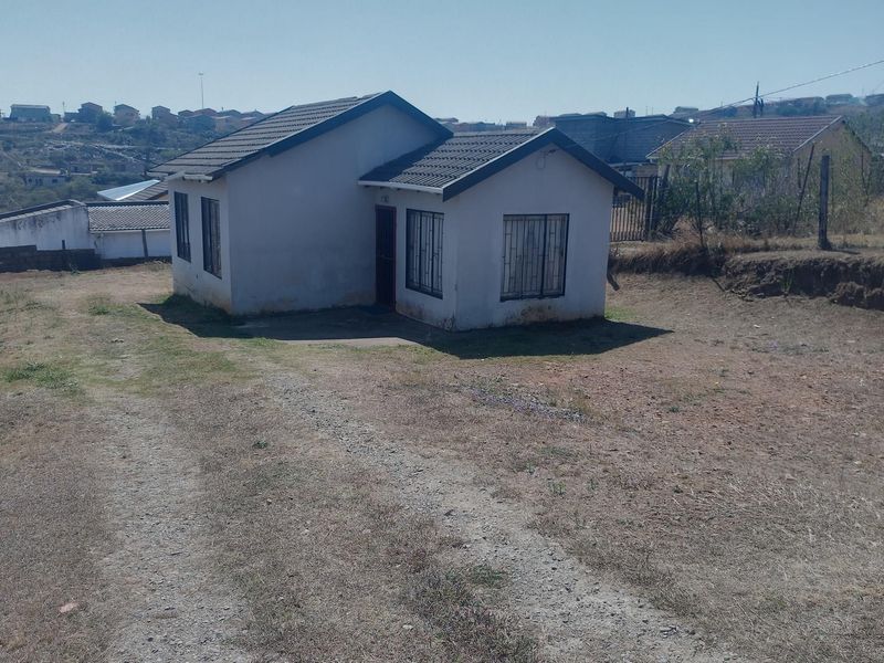 A detached single-story house featuring a tiled roof and security bars on windows, situated on a large plot with an unpaved driveway.