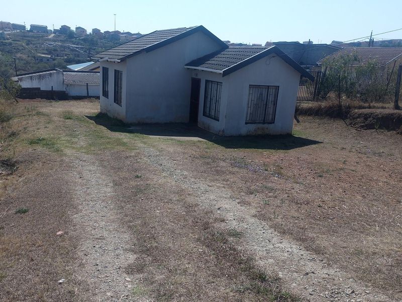 A detached single-story house featuring a tiled roof and security bars on windows, situated on a large plot with an unpaved driveway.