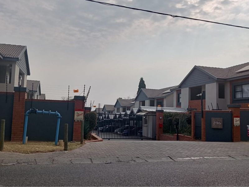 Front entrance view of a residential apartment complex featuring a secure gated access point, brick boundary walls, and paved driveway.