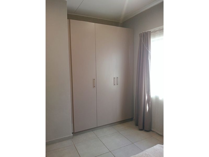 A clean bedroom featuring neutral tiled flooring and a large, modern built-in wardrobe with sleek handles.
