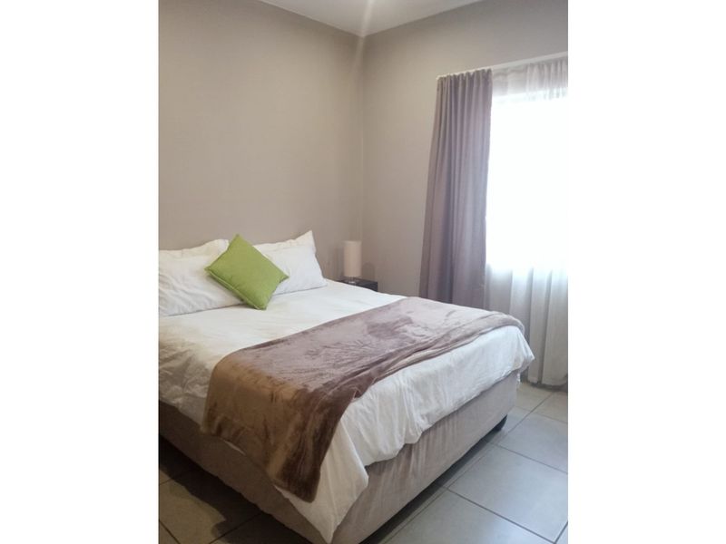 A neutrally painted bedroom featuring tiled flooring and natural light through a window with installed curtain tracks.