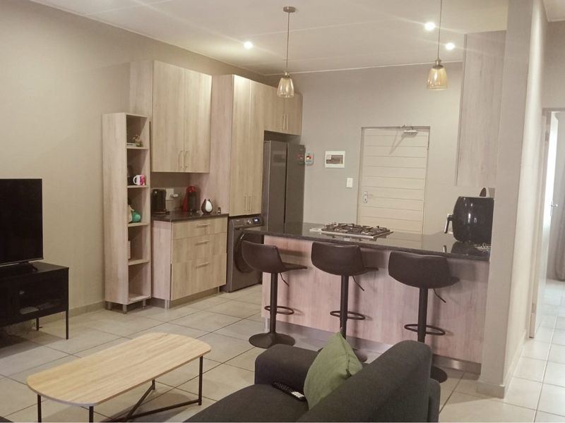 Modern open-plan living area featuring a well-appointed kitchen with light wood cabinetry, granite countertops, and a breakfast bar with integrated gas hob.