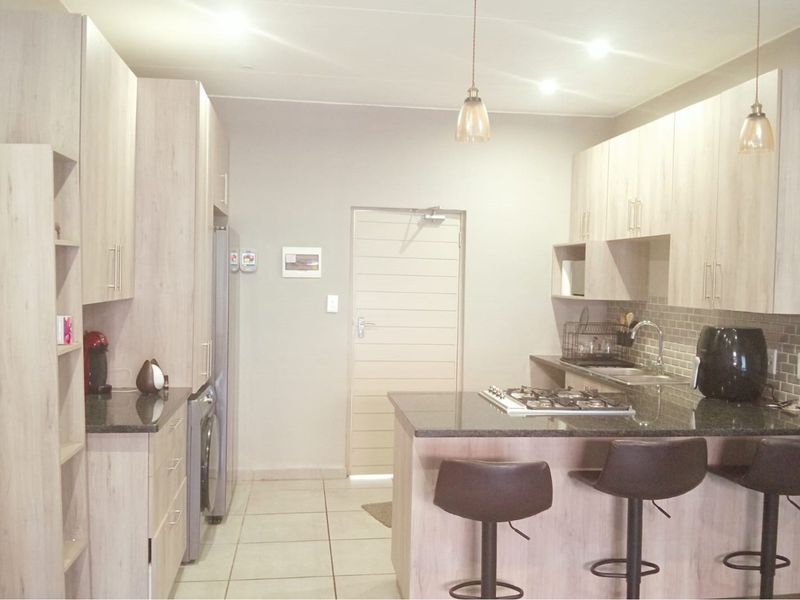 Modern kitchen featuring light wood-finish cabinetry, granite countertops, a gas hob, and a tiled backsplash, offering a functional and contemporary cooking space.