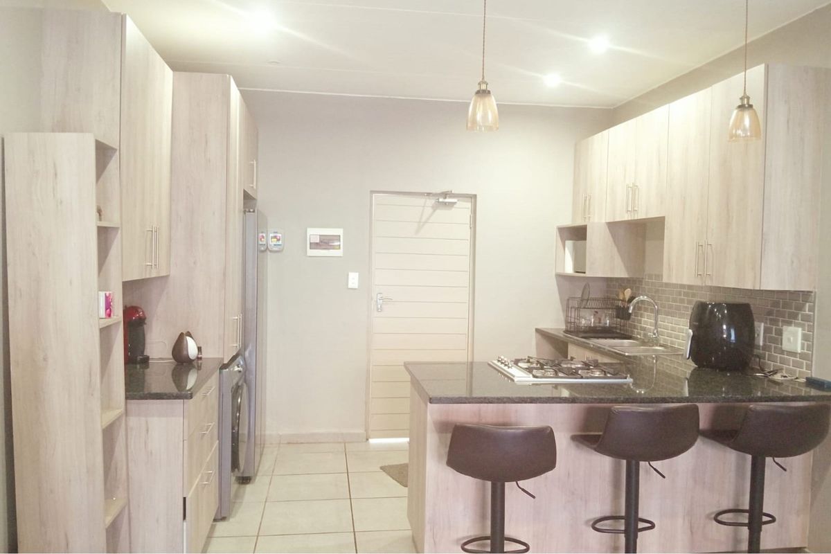 Modern kitchen featuring light wood-finish cabinetry, granite countertops, a gas hob, and a tiled backsplash, offering a functional and contemporary cooking space.