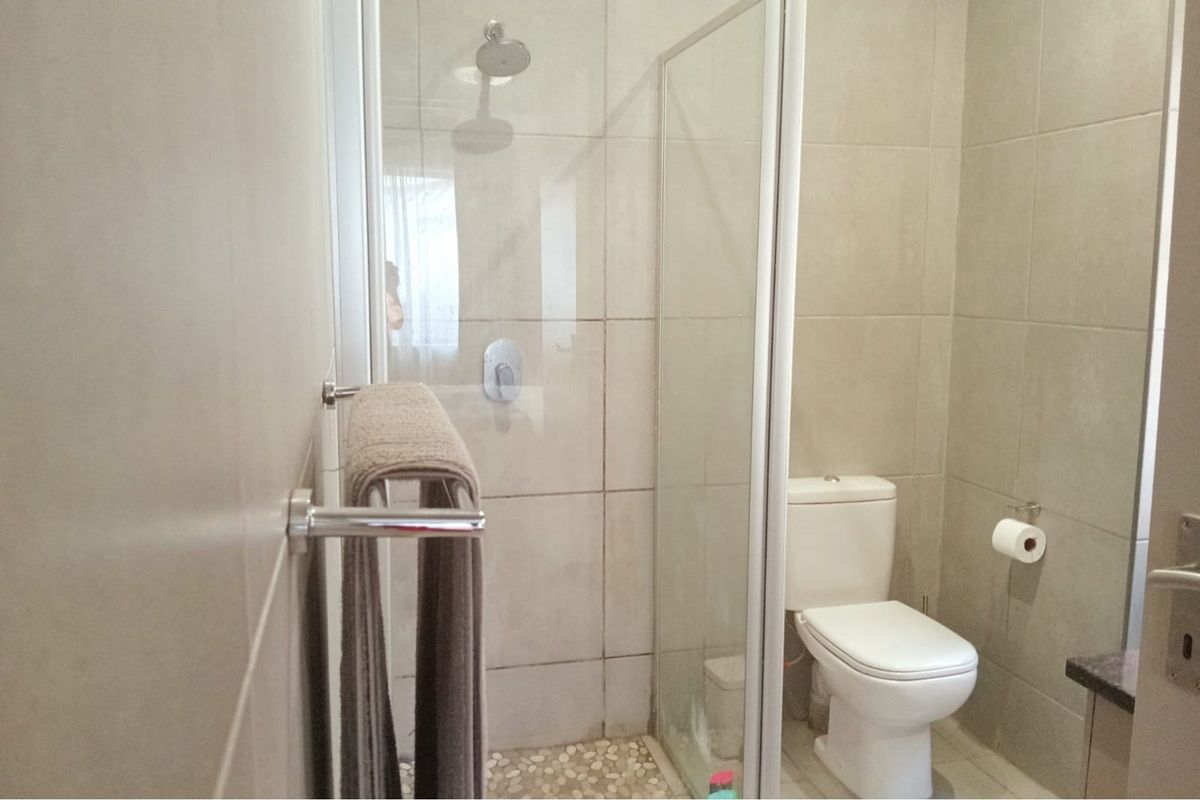 A functional bathroom featuring a walk-in shower with a glass screen, a toilet, and neutral wall and floor tiling.