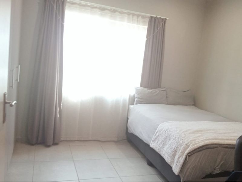 A simple bedroom featuring tiled flooring and a built-in wardrobe, illuminated by natural light from a large window.