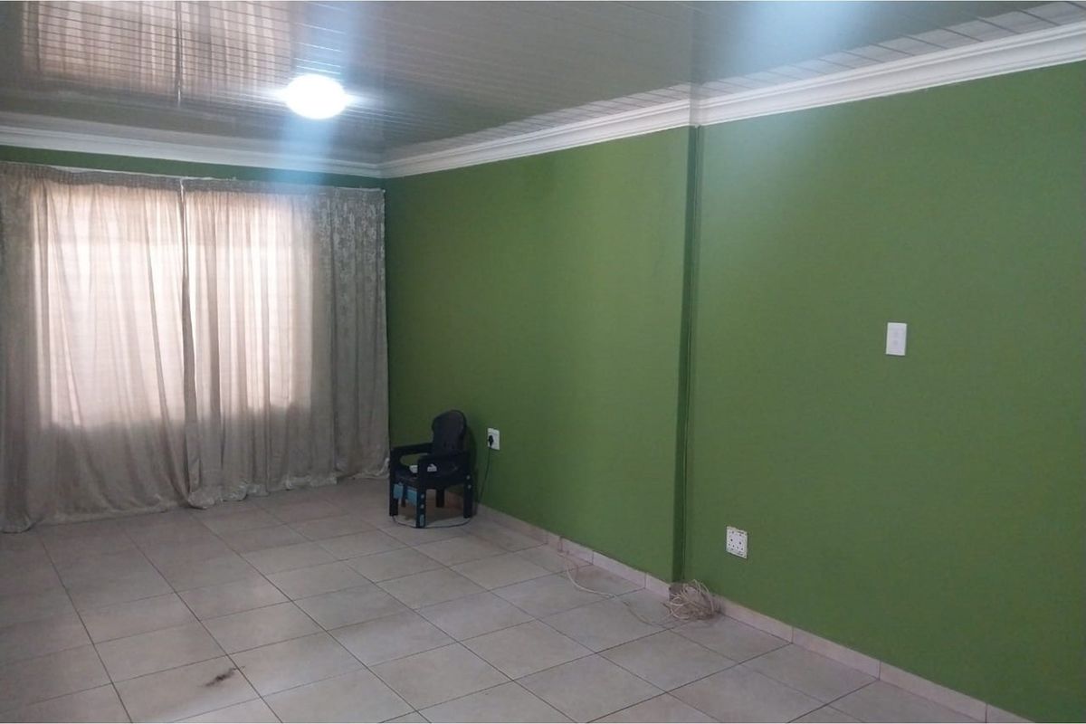 A spacious living room featuring tiled flooring, green painted walls, and a glossy ceiling finish with crown molding.