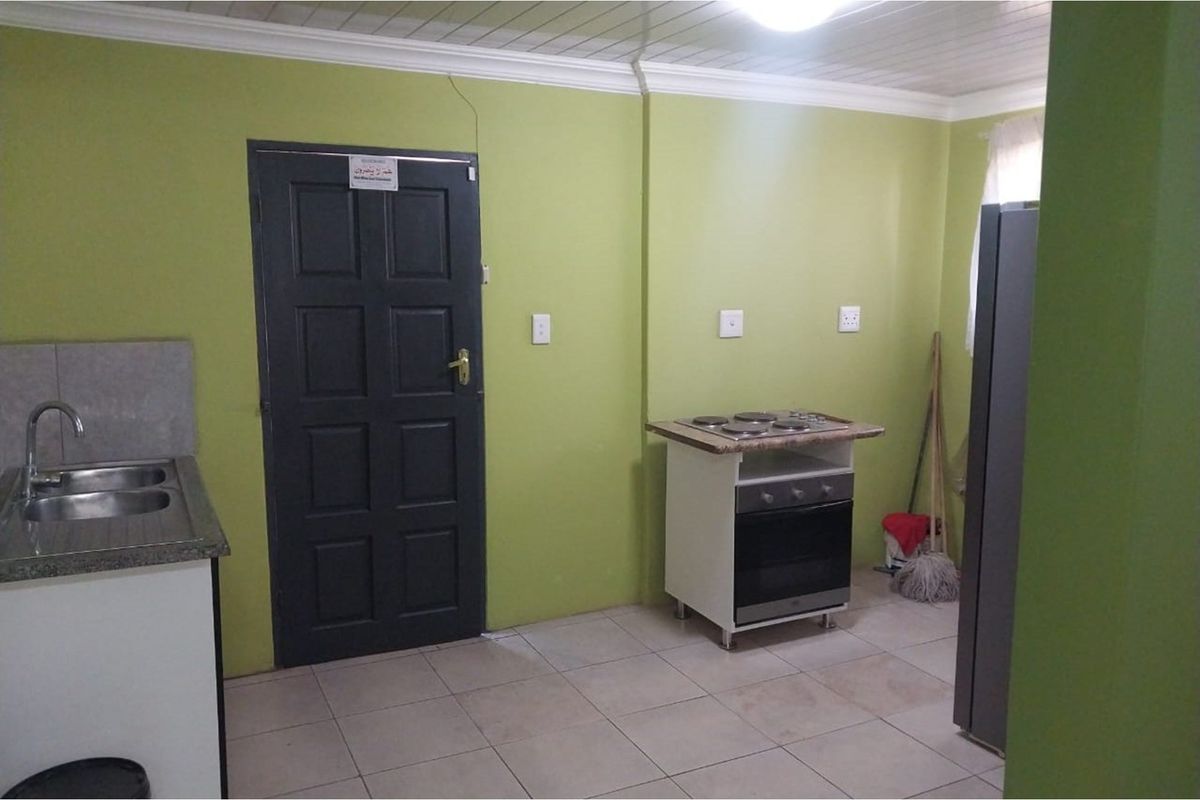 A functional kitchen area featuring a built-in sink, tiled flooring, and a freestanding stove unit against lime green walls.