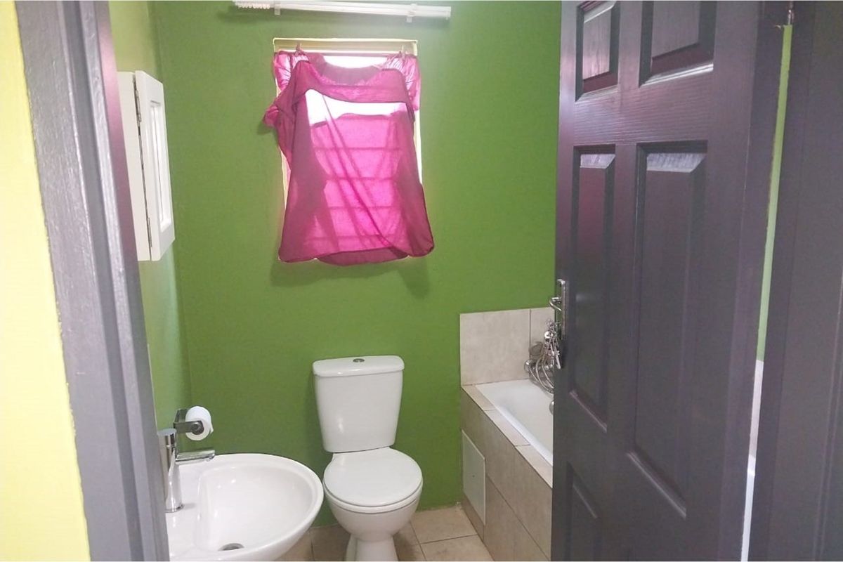 A compact bathroom featuring a white toilet, pedestal basin, and a tiled bathtub with a window.