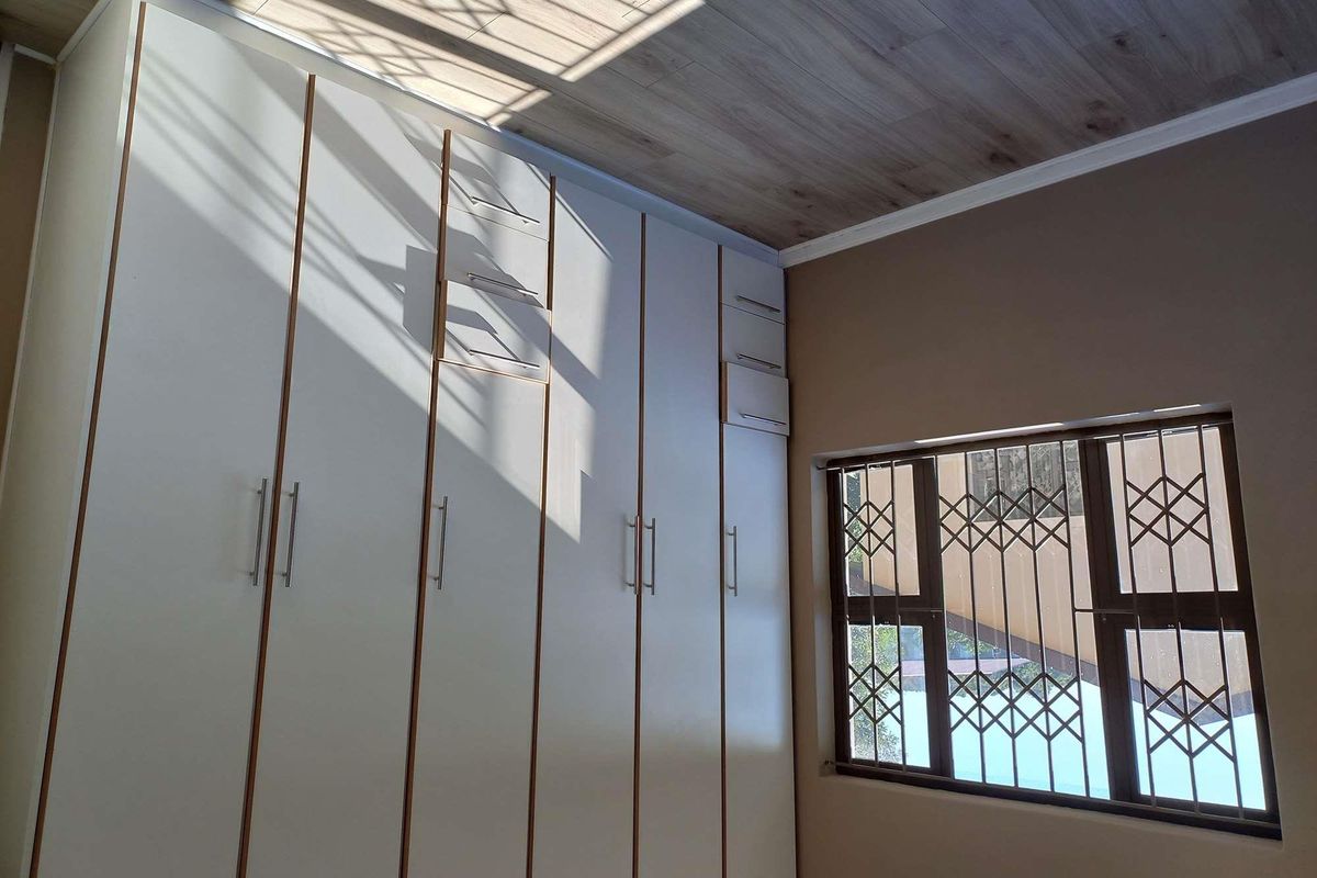 Bedroom featuring floor-to-ceiling built-in cabinetry with modern handles and a window fitted with security bars.