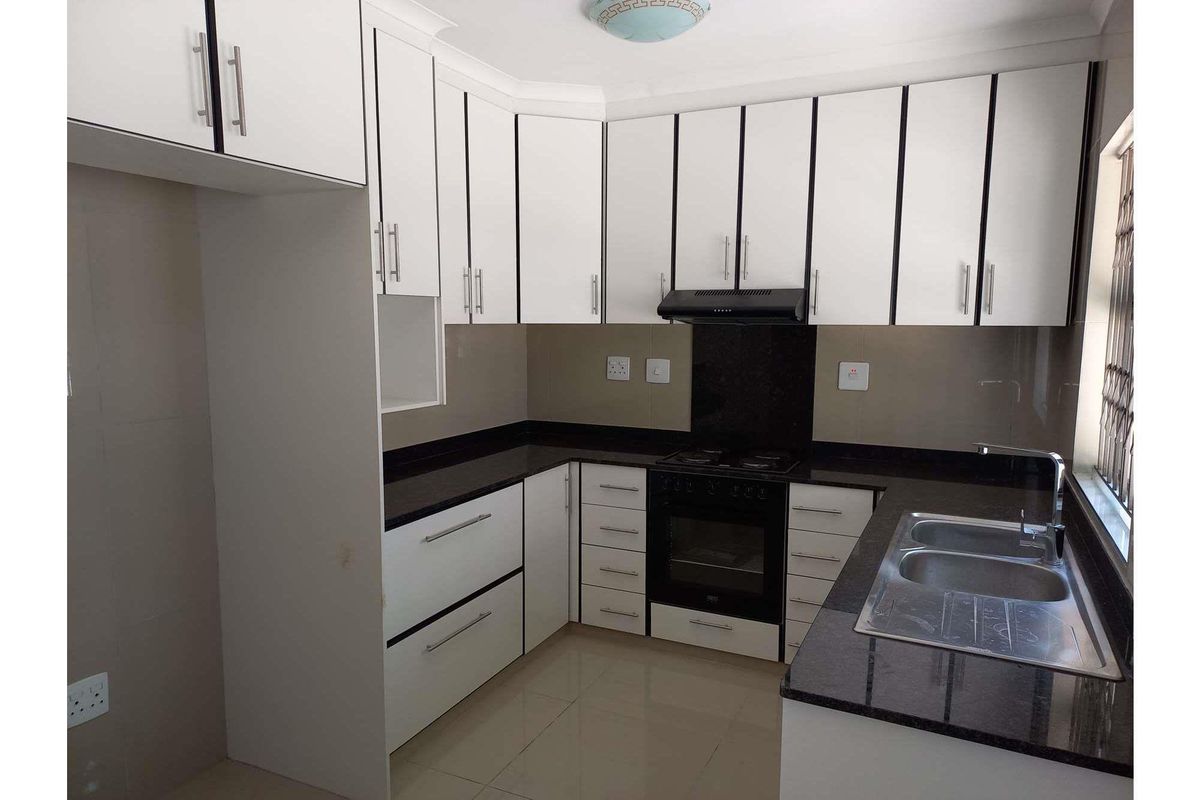 A clean, modern kitchen featuring white cabinetry, dark granite countertops, a built-in oven with extractor fan, and a double bowl stainless steel sink.