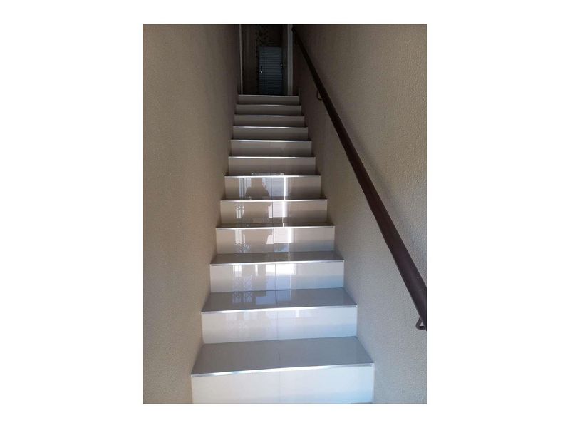 A straight staircase featuring modern white tiled steps and a dark metal handrail against textured walls.
