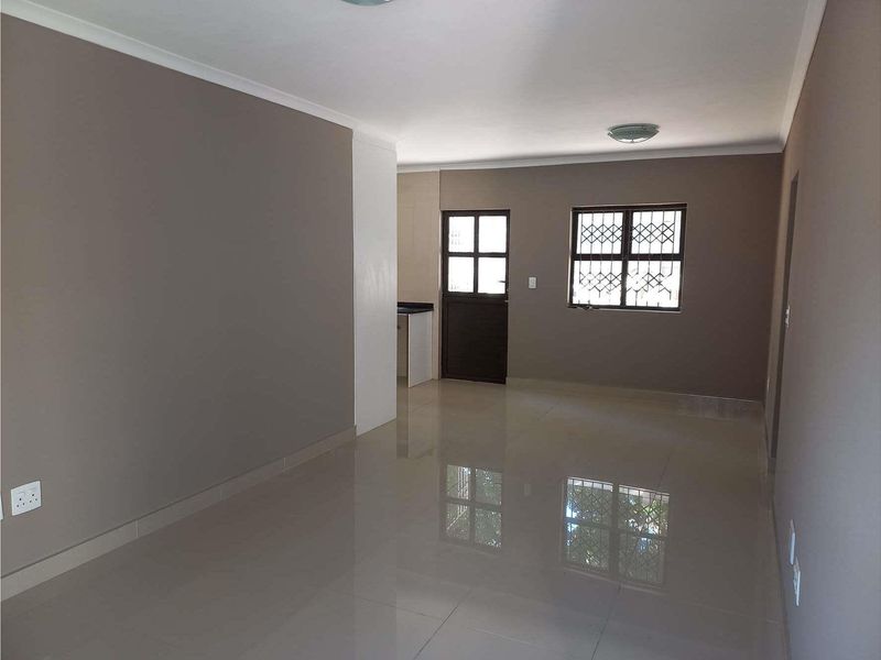 An open-plan living area featuring polished tiled flooring, neutral wall tones, and secure window and door access.