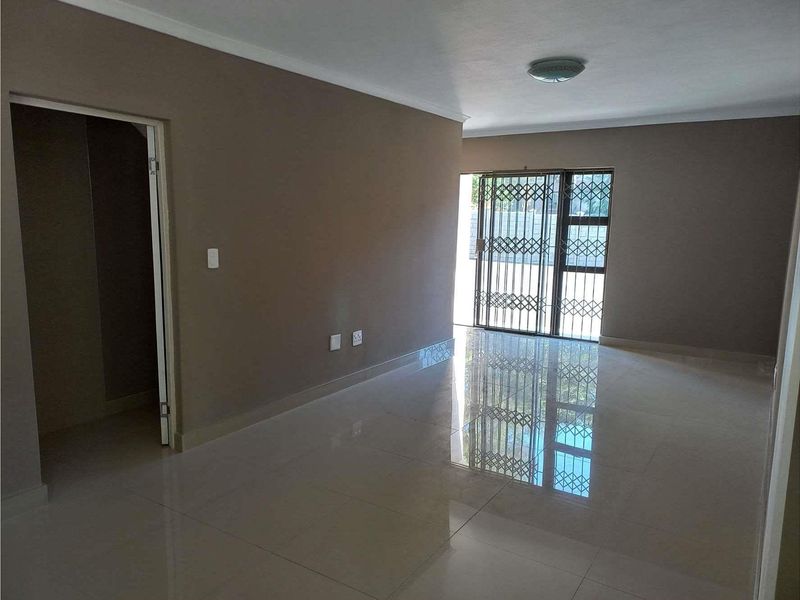 A spacious, empty living room featuring neutral wall tones, polished tiled flooring, and a sliding glass door with a security gate leading outdoors.
