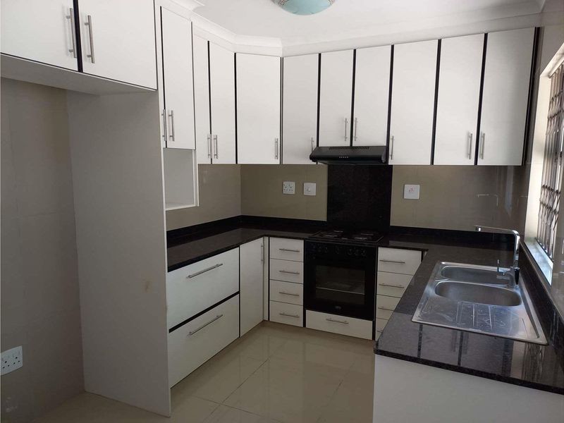 Modern kitchen featuring white cabinetry, dark granite countertops, built-in oven, gas hob, extractor fan, and a double bowl stainless steel sink.