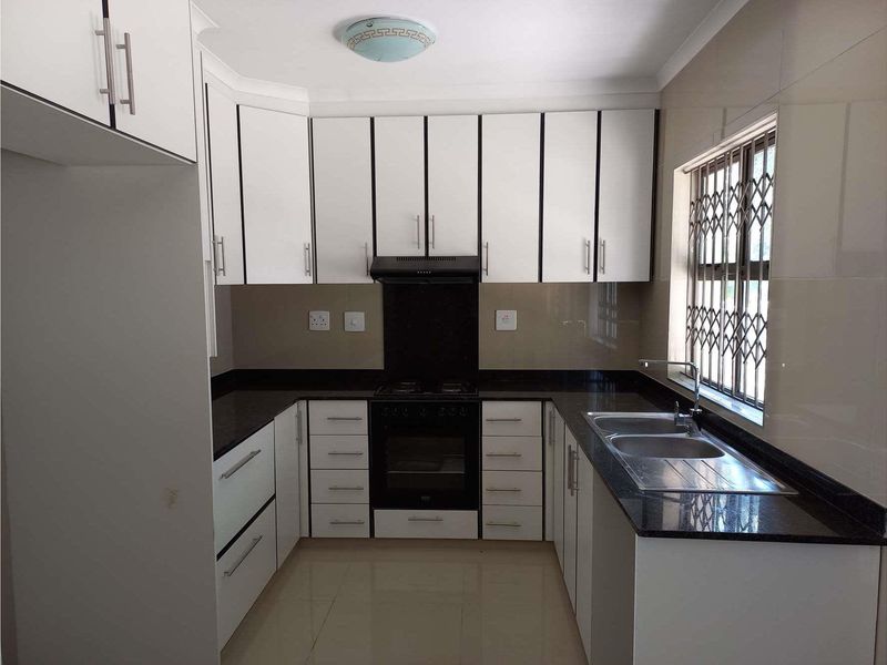 A clean, modern kitchen featuring white cabinetry, dark granite countertops, a double basin sink, and a built-in oven with an extractor fan.