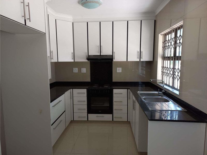 A clean, modern kitchen featuring white cabinetry, dark granite countertops, a built-in oven with gas hob, and a double sink with a window view.