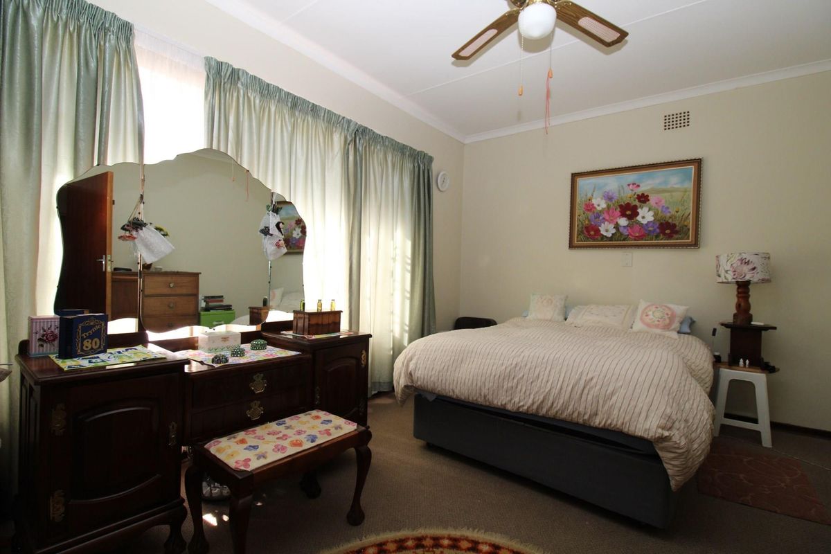 A bedroom featuring a ceiling fan, carpeted flooring, and large windows with curtains.