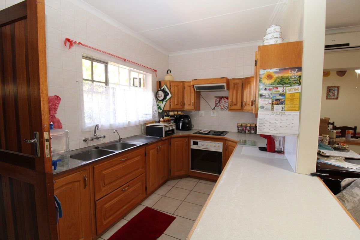 Functional kitchen featuring wooden cabinetry, built-in oven, hob, extractor fan, and double stainless steel sink with tiled splashbacks.