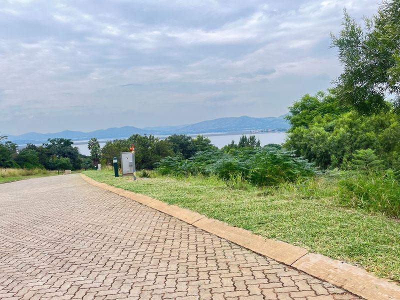 A view of a paved residential street leading towards a scenic landscape with distant mountains and water.