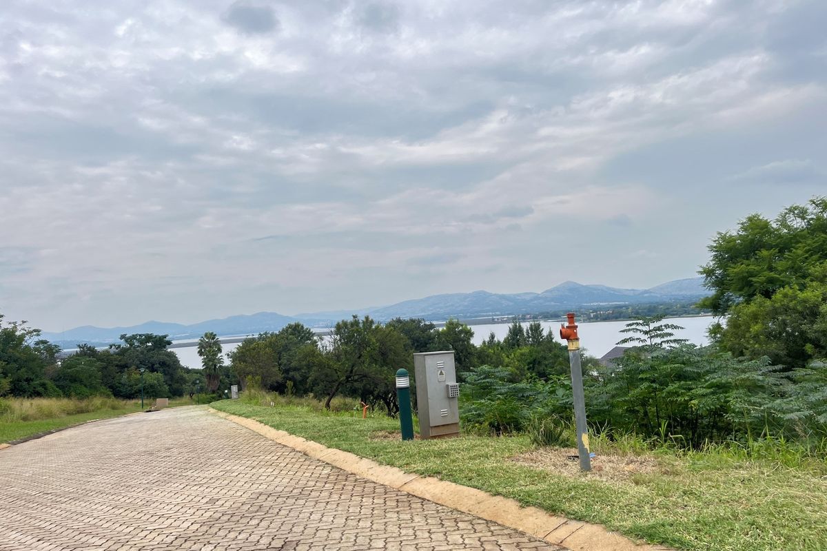 A view of a paved residential driveway leading towards a scenic landscape with water and mountain views.