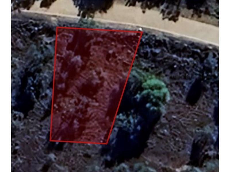 An aerial view of a vacant residential plot, highlighted with a red boundary overlay, showing the natural terrain and surrounding vegetation.