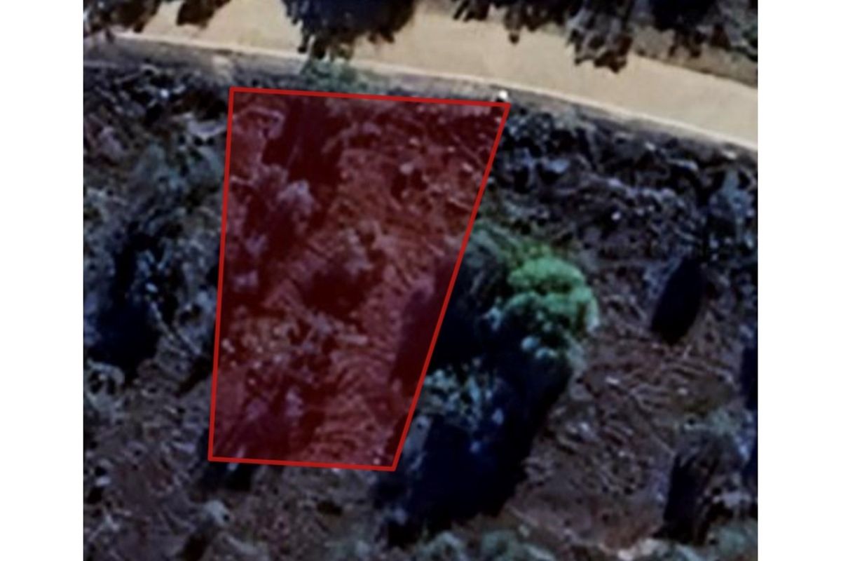 An aerial view of a vacant residential plot, highlighted with a red boundary overlay, showing the natural terrain and surrounding vegetation.