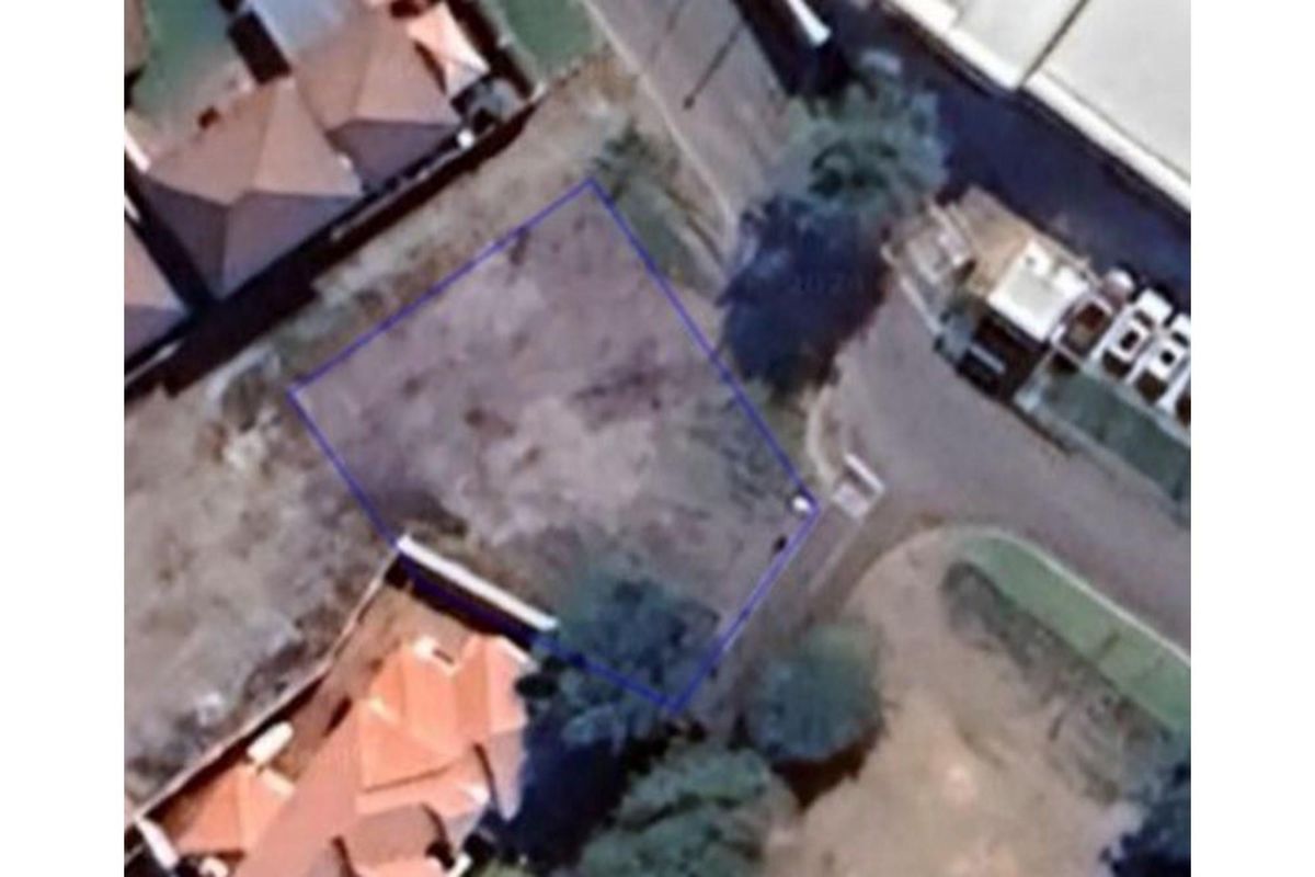 An aerial view of a vacant residential plot of land, clearly outlined in blue, situated within an established neighborhood.