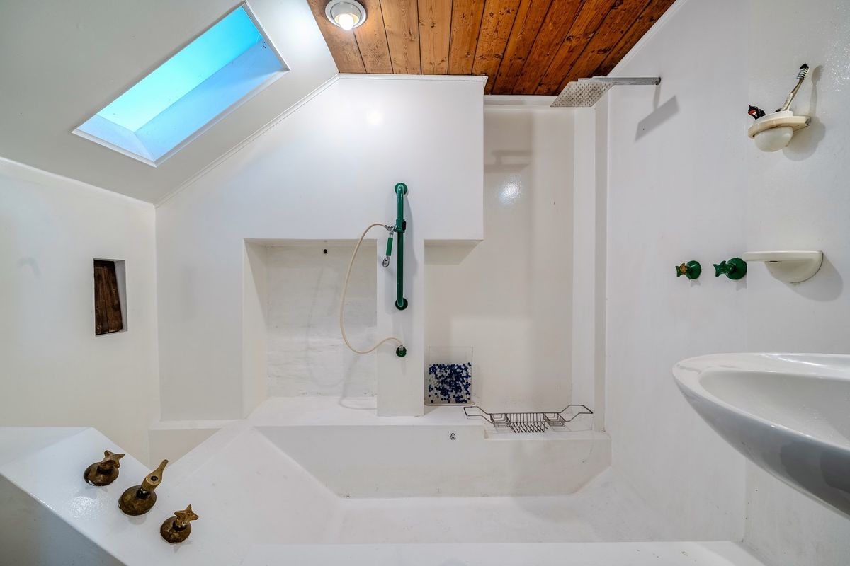 A dated bathroom featuring a built-in bathtub, shower head, skylight, and timber-paneled ceiling, offering potential for a modern renovation.