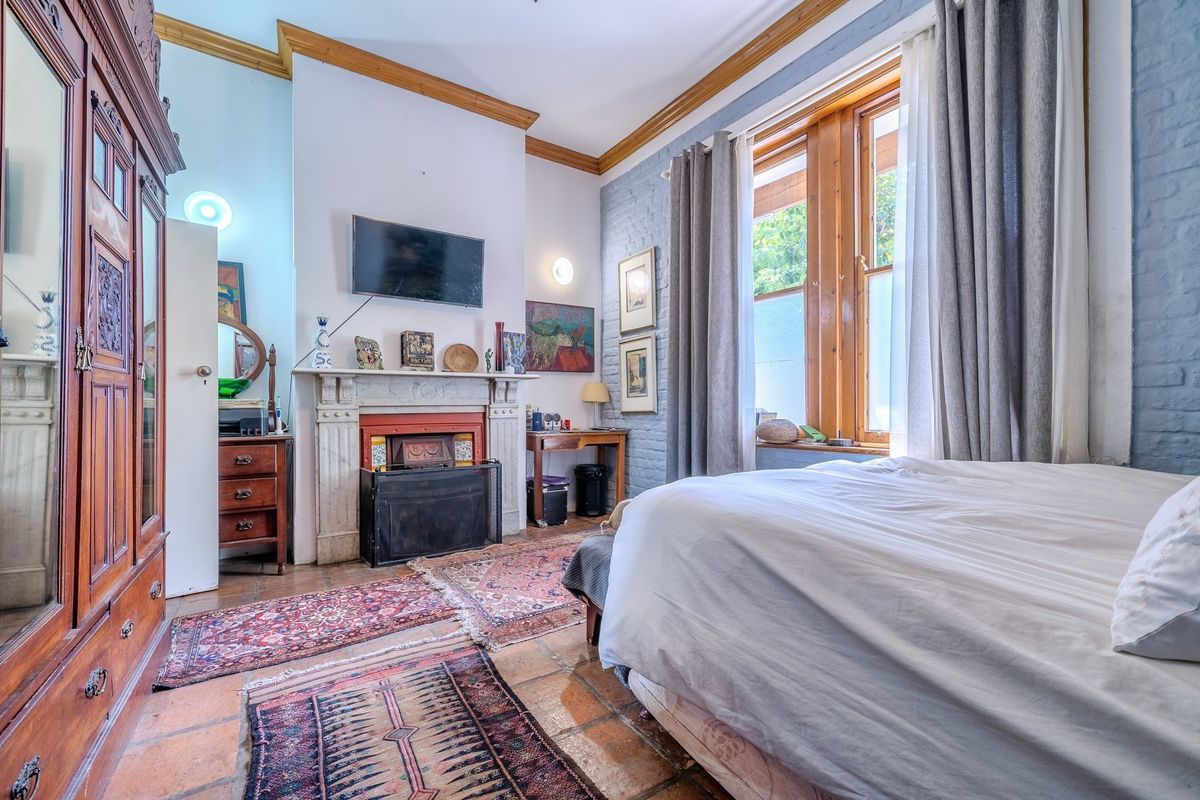 A character-filled bedroom featuring a classic fireplace, exposed brick walls, timber window frames, and traditional terracotta floor tiles.