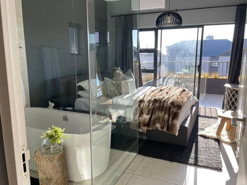 Modern bedroom featuring an open-plan ensuite with a freestanding bathtub, glass partition, split-system air conditioning, and direct access to a private balcony.