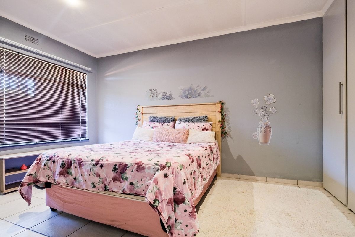 A bedroom featuring tiled flooring, built-in cupboards, and a window fitted with venetian blinds.