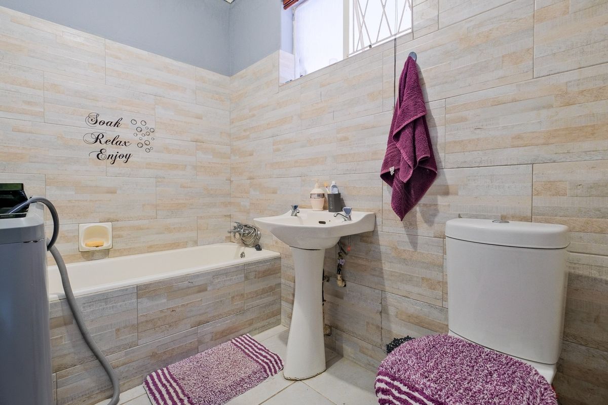 A functional bathroom featuring a pedestal basin, a standard bathtub with wall-mounted mixer, and a close-coupled toilet with full-height wall tiling.