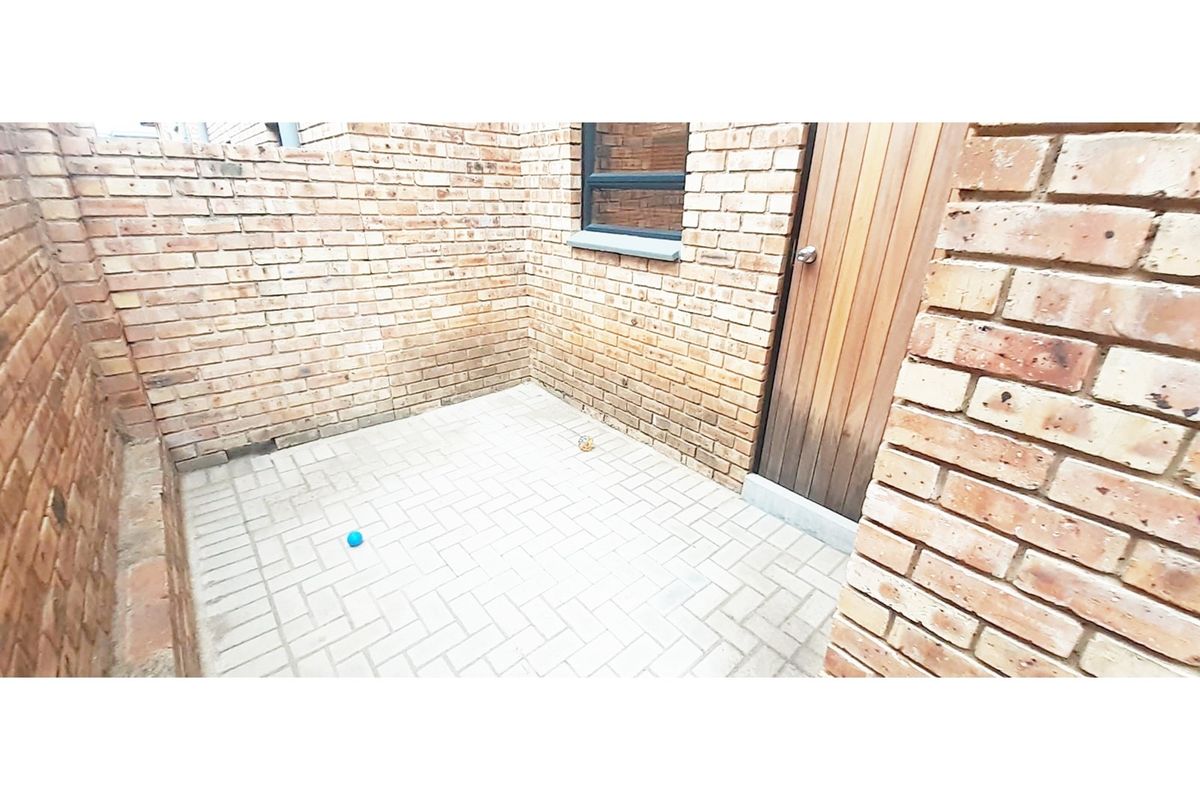 A private, enclosed courtyard featuring exposed brick walls, paved flooring, and a wooden door providing access to the property.