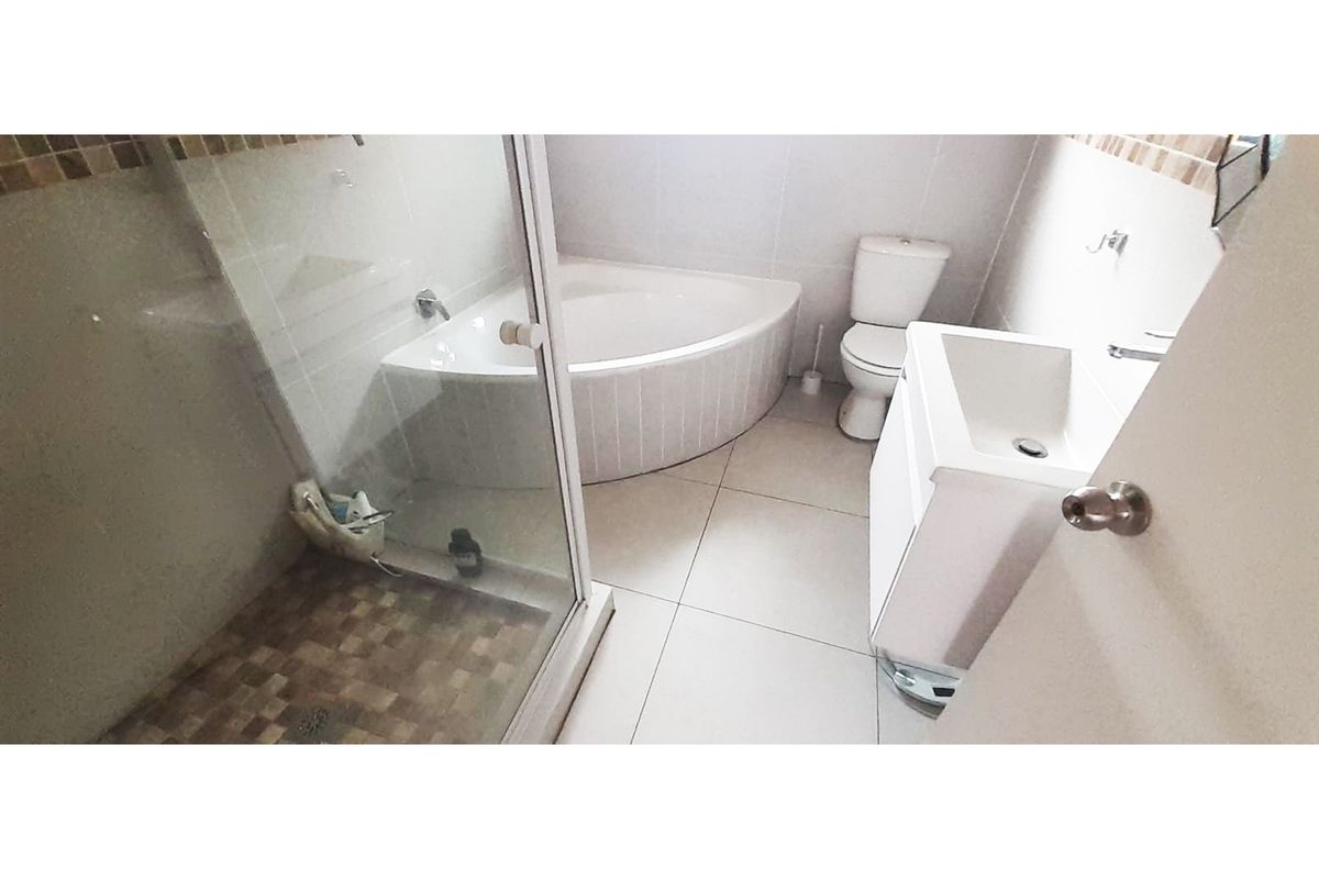 A functional bathroom featuring a corner bathtub, a separate glass-enclosed shower, a modern vanity, and a toilet with tiled flooring.