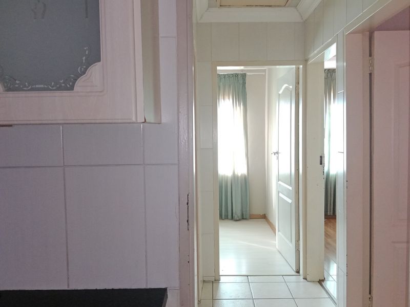 A view through a hallway showing tiled flooring, internal doors, and built-in cabinetry, leading towards a bright bedroom area.