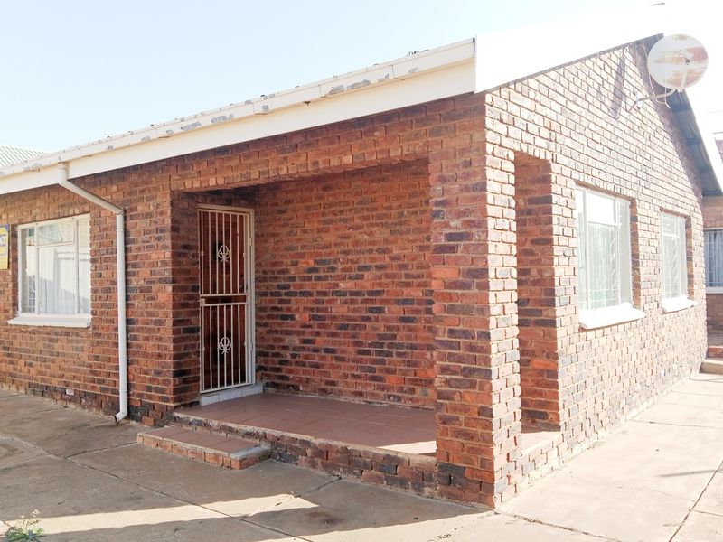 A single-story face brick house featuring a covered front porch, security gates, and window bars, presenting a classic and durable exterior finish.