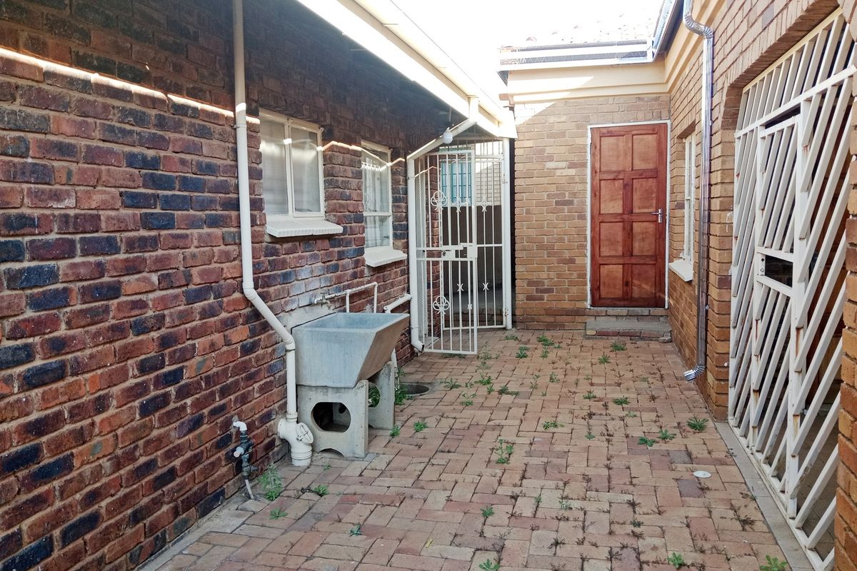 A paved rear courtyard area featuring a concrete wash trough, security gates, and exposed brick walls, requiring some maintenance to clear weeds.