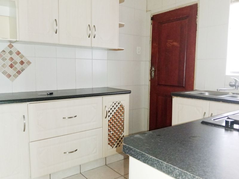 A functional kitchen featuring white built-in cabinetry, dark laminate countertops, tiled backsplash, and a stainless steel sink.