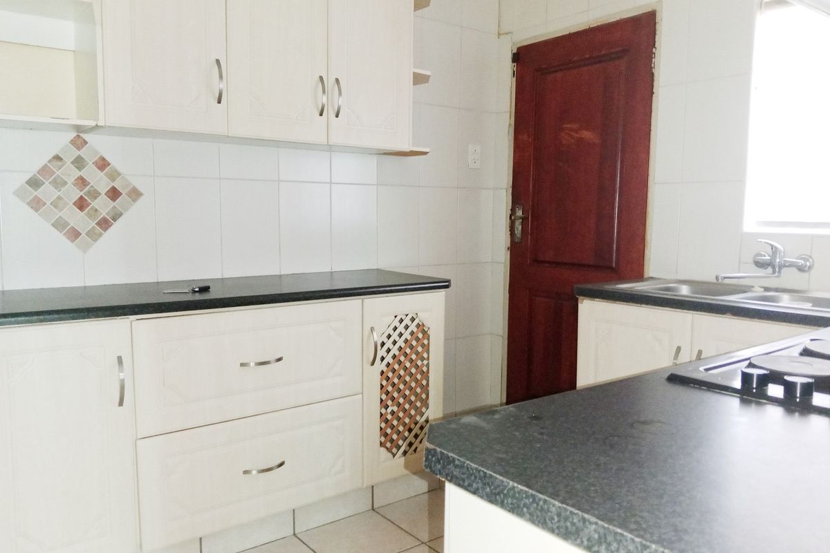 A functional kitchen featuring white built-in cabinetry, dark laminate countertops, tiled backsplash, and a stainless steel sink.