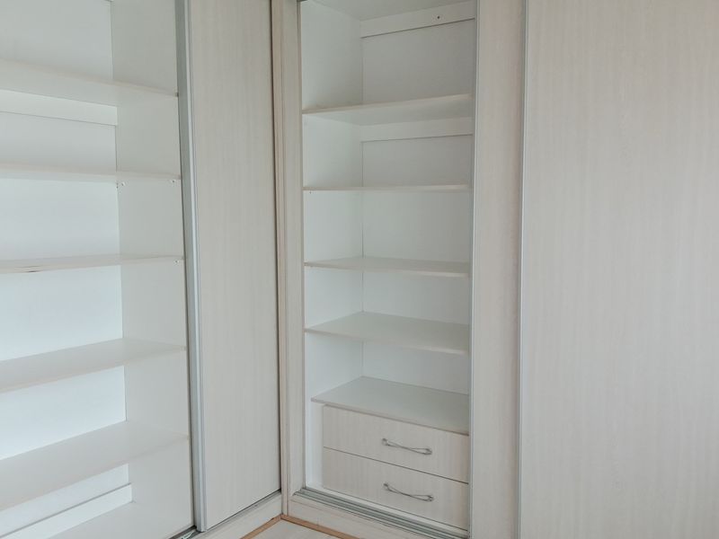 A view of built-in bedroom cupboards featuring light wood-grain finish, integrated shelving, and lower storage drawers.