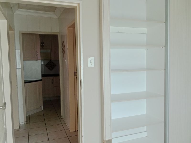 A hallway featuring built-in shelving and tiled flooring, providing a view into the adjacent kitchen area.