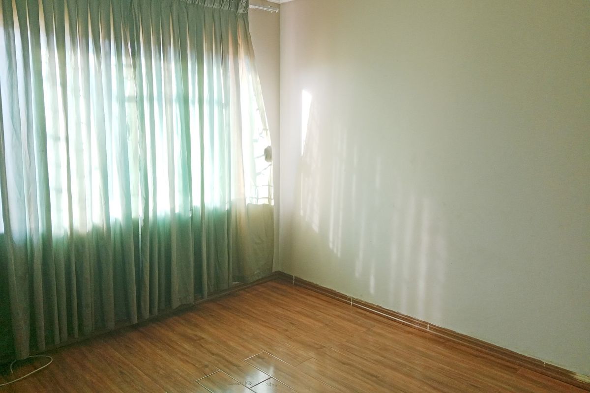 A vacant bedroom featuring laminate flooring and large windows with curtains, offering a blank canvas for personalization.