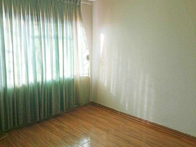 A vacant bedroom featuring laminate flooring and large windows with curtains, offering a blank canvas for personalization.