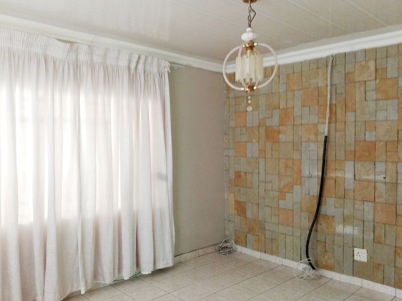 An empty living room featuring a stone-clad feature wall, ceramic floor tiles, and a decorative pendant light fixture.