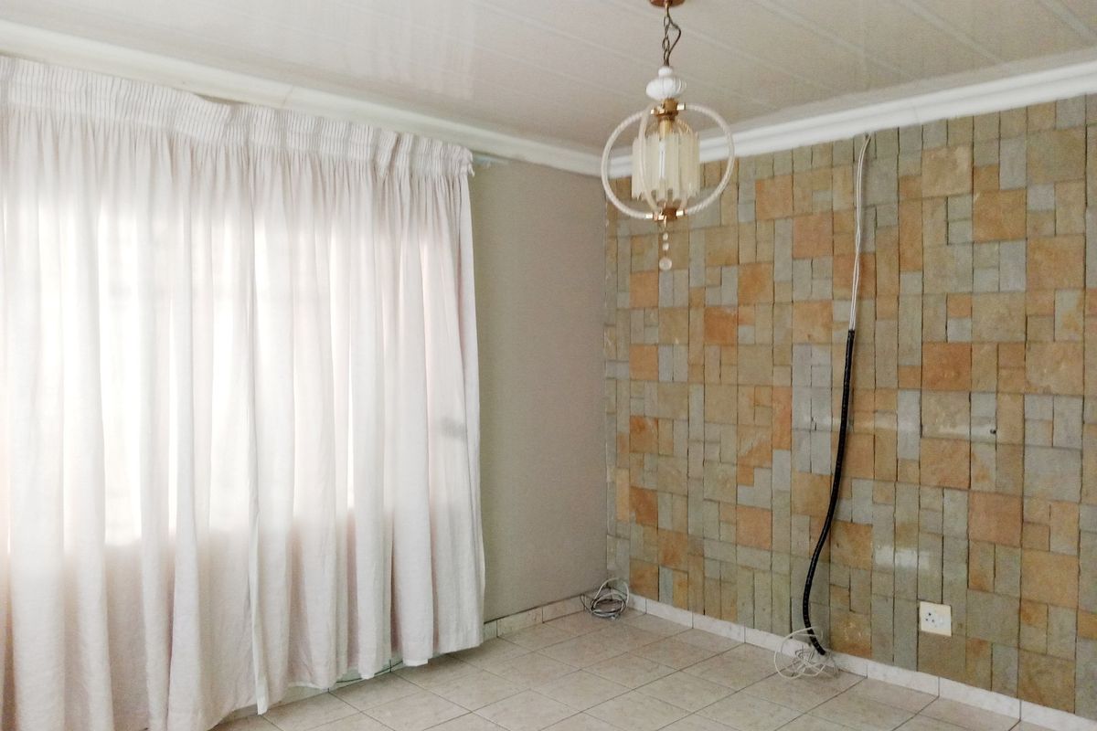An empty living room featuring a stone-clad feature wall, ceramic floor tiles, and a decorative pendant light fixture.