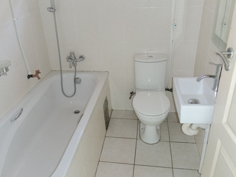 Compact bathroom featuring a bathtub with shower mixer, a standard toilet, and a wall-mounted basin with tiled finishes.