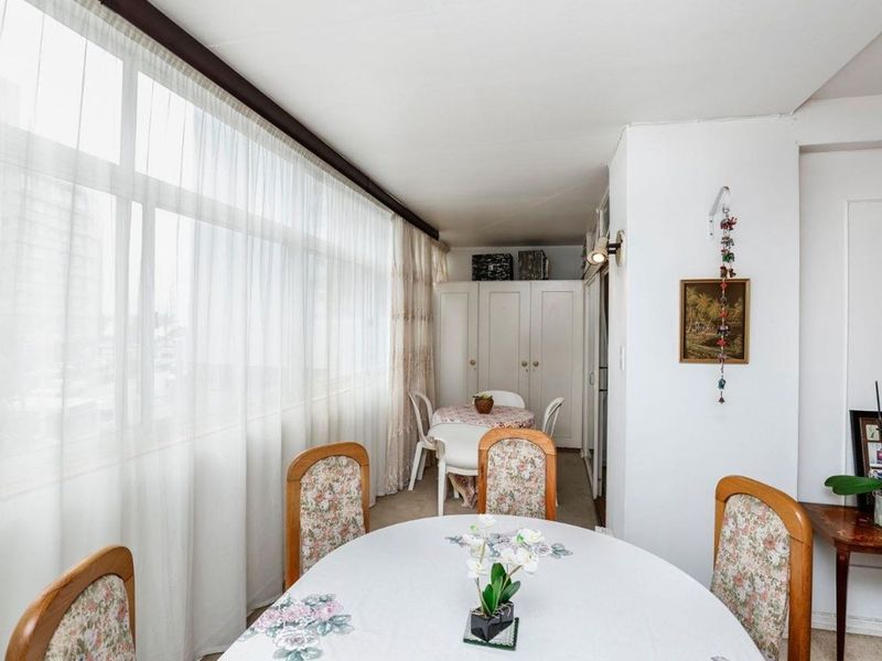 A sun-drenched enclosed balcony or sunroom featuring large windows, built-in storage cabinetry, and neutral carpeting, suitable for a dining or relaxation area.