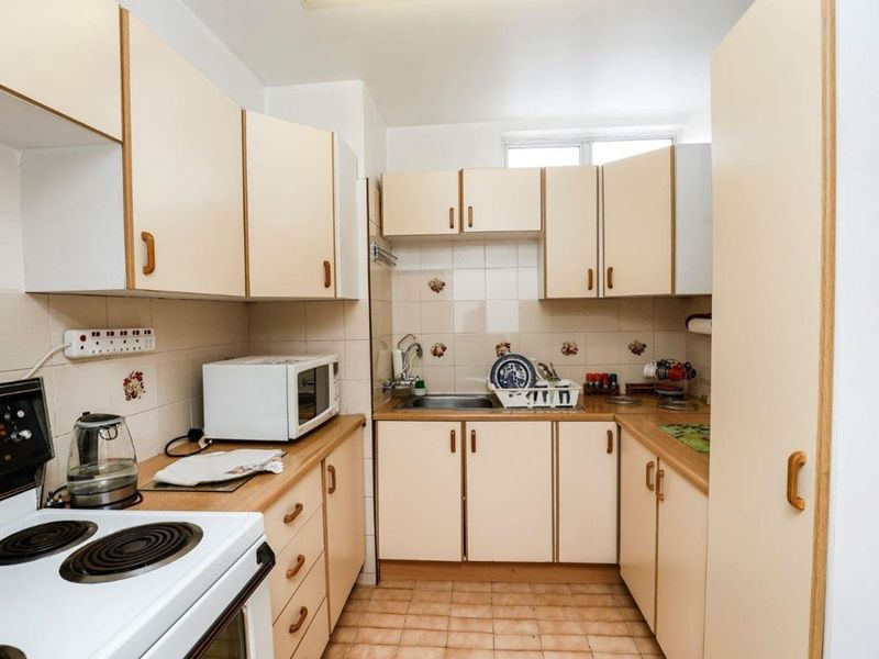 A compact, dated kitchen featuring laminate cabinetry, tiled splashbacks, and a functional electric stove, offering potential for a modern renovation.